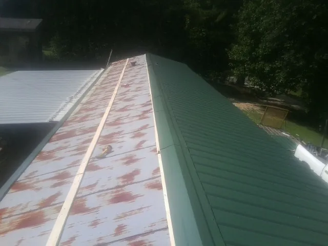 Old rusted panels beside newly installed green metal roofing — Wind Damage Roof Repair by Roofing Brothers in Beulah