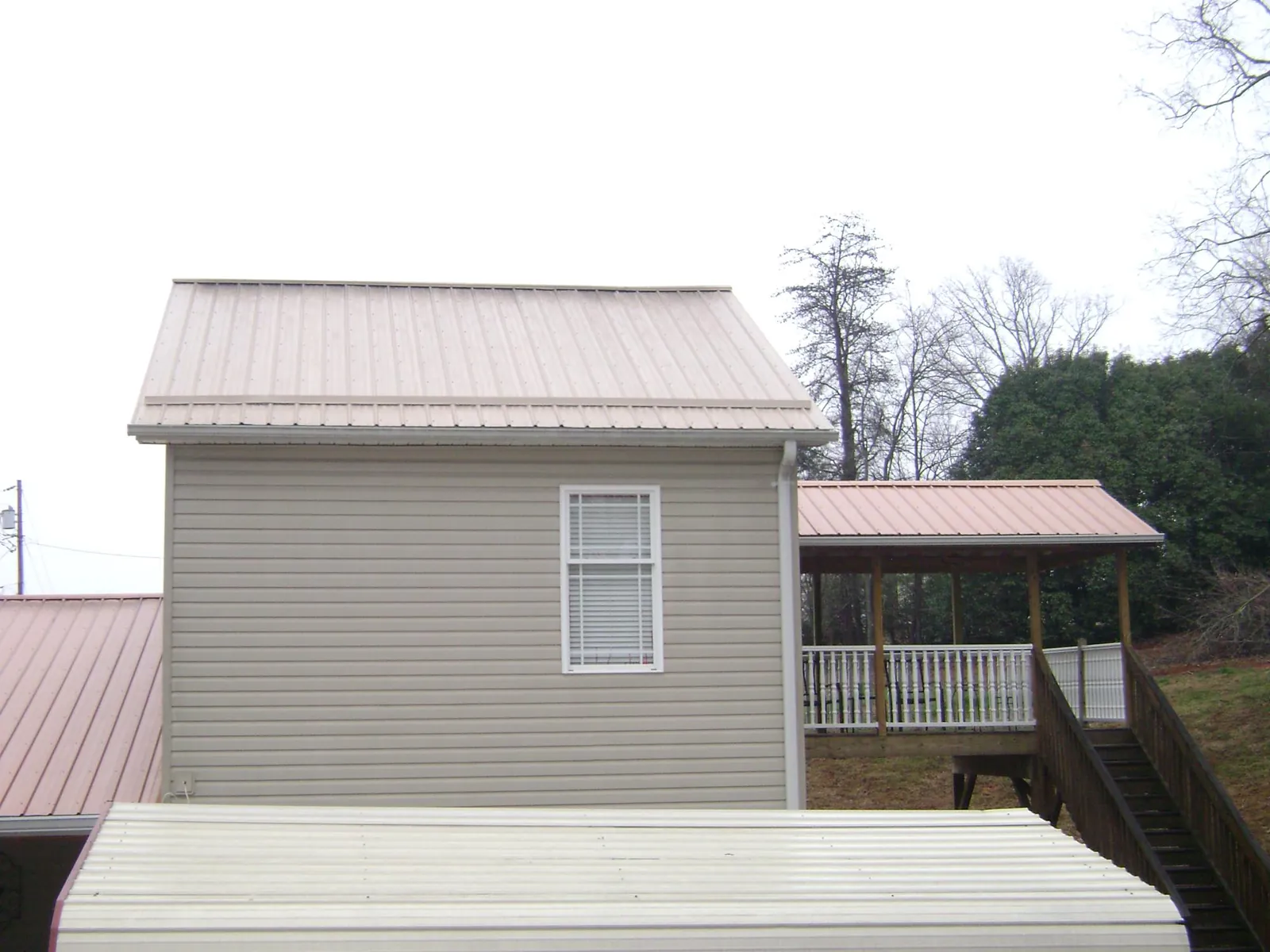 Tan metal roofs on a two story addition and attached porch, from a Roof Replacement job in Beulah